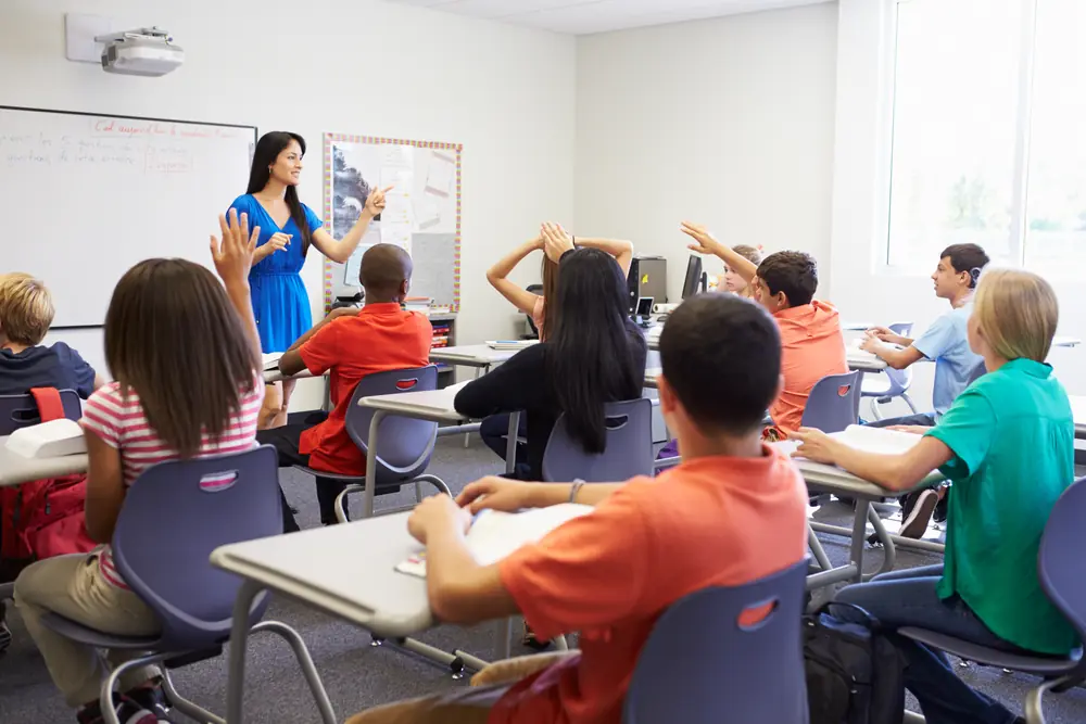 A classroom of students raising their hands